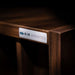 GIK Acoustics Q11D Quadratic Residue Diffuser close-up showing the product badge attached to the edge of a rich walnut-finished diffuser panel