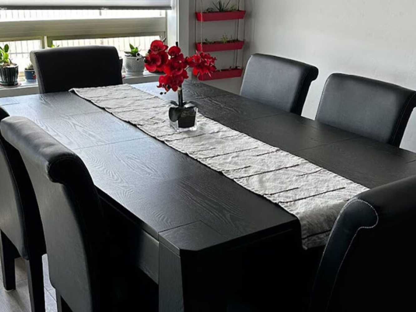 Game Theory Tables Origins Lit Game Table serves as an elegant black dining table, adorned with a light table runner and a small flower centerpiece