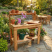 Garden patio shows a potting bench with flowers, tools, and soil, with Outdoor Living Today 4×2 Western Red Cedar Potting Bench at the center