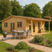 GardenHouse24 USA Bente 70 Garden Room features a charming log-style exterior with an outdoor dining area and barbecue grill in a lush garden
