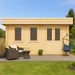 GardenHouse24 USA Miriam 44B Classic Garden Room is shown in a cozy garden setting with a wicker chair set, hammock swing, and lush greenery, enhancing its inviting wooden exterior