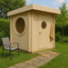 GardenHouse24 USA Sauna Maria 90 Garden Room is placed on a grassy lawn with a stone path, featuring a round window and door with circular glass
