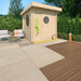 GardenHouse24 USA Sauna Maria 90 Garden Room sits on a sunny patio surrounded by greenery, with a towel hanging outside and round windows visible