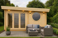 GardenHouse24 USA Sauna Tanonka 70 Garden Room is shown lit at dusk with cozy outdoor wicker furniture and soft wall lighting