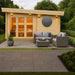 GardenHouse24 USA Sauna Tanonka 70 Garden Room is shown lit at dusk with cozy outdoor wicker furniture and soft wall lighting