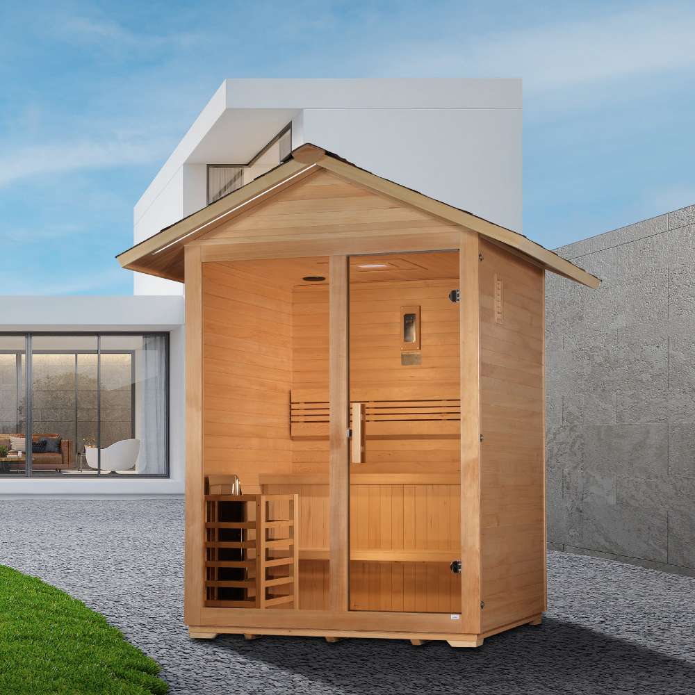 Golden Designs Arlberg 3 Person Traditional Outdoor Sauna stands on a gravel courtyard beside a lawn in front of a modern white building