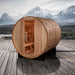 Golden Designs Arosa 4 Person Barrel Traditional Sauna on a wooden deck with snowy mountains and a cloudy sky behind it