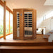 Golden Designs Dynamic Heming 2 Person Low EMF Far Infrared Corner Sauna sits in the corner of a sunlit room with a wood floor and large windows