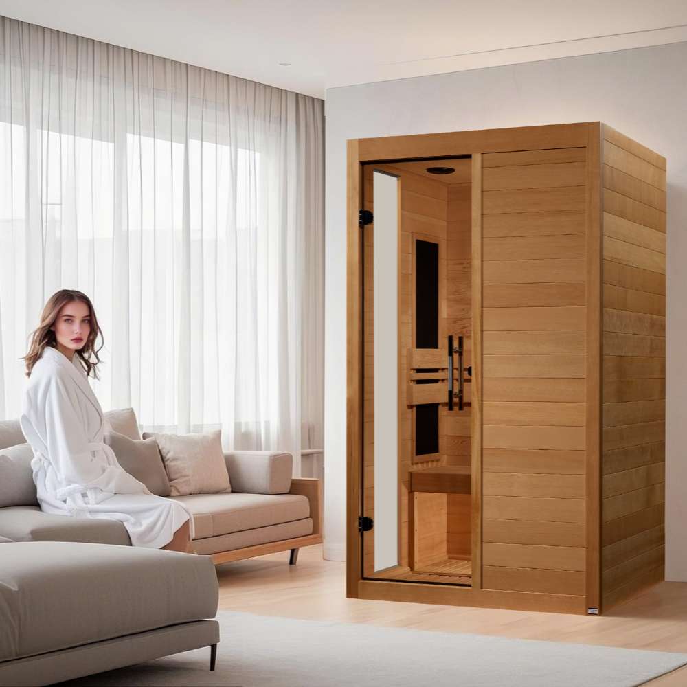 Golden Designs Dynamic Lucca Elite 2 Person Ultra Low EMF Far Infrared Sauna stands in a bright living room beside a sofa where a woman in a white robe relaxes