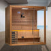 Golden Designs Forssa 3-4 Person Traditional Sauna stands on a wood floor in a bright room with a gray wall and a window overlooking the sea