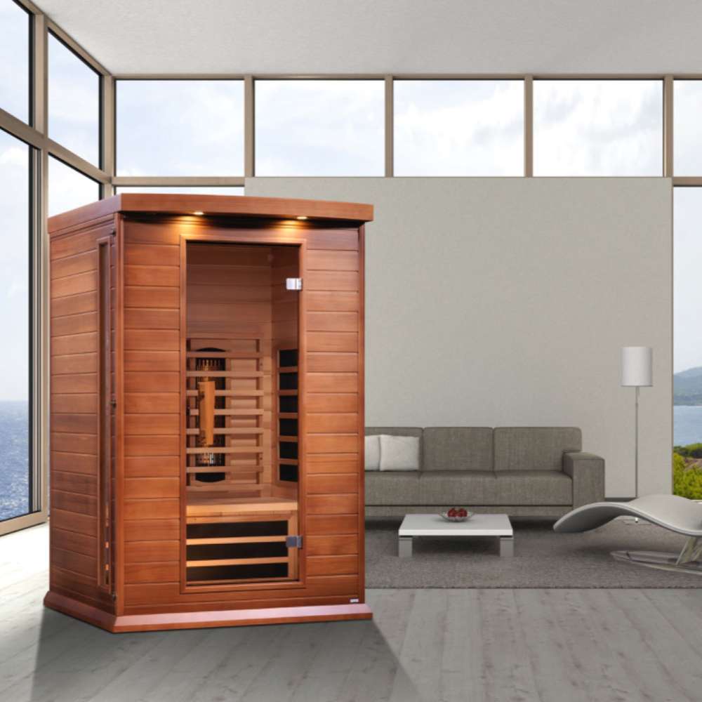 Golden Designs Maxxus 2 Person Full Spectrum Infrared Sauna in Red Cedar stands in a modern room with large windows, a gray sofa and coffee table