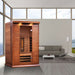 Golden Designs Maxxus 2 Person Full Spectrum Infrared Sauna in Red Cedar stands in a modern room with large windows, a gray sofa and coffee table