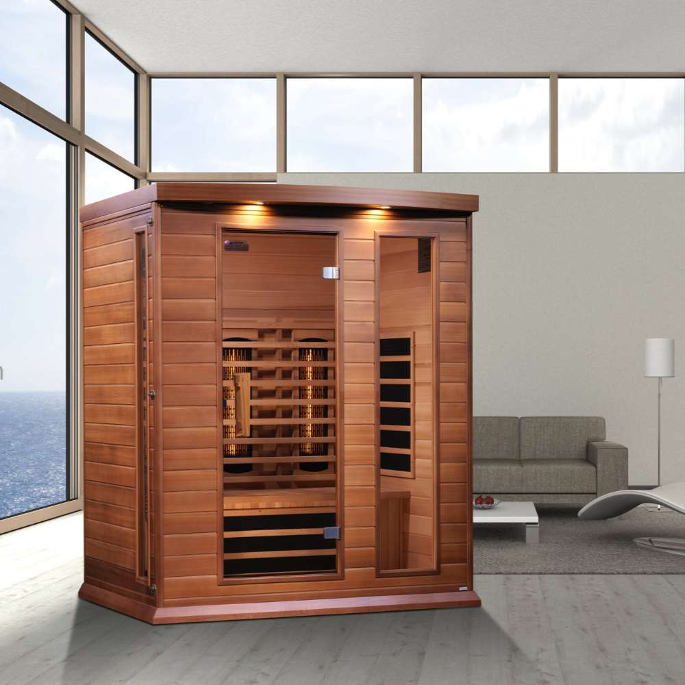 Golden Designs Maxxus 3 Person Full Spectrum Infrared Sauna in Red Cedar stands in a bright room with large windows and a gray sofa