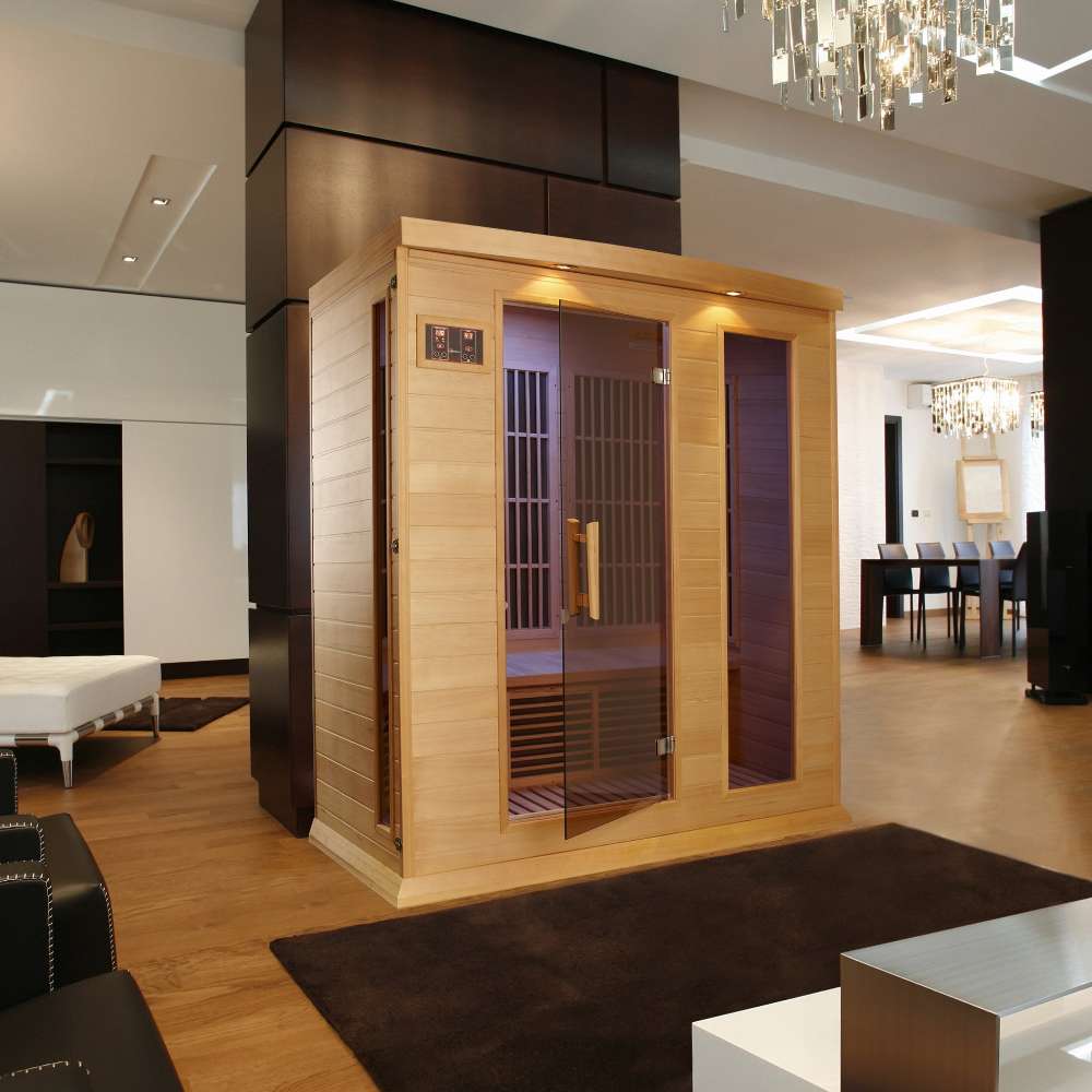 Golden Designs Maxxus 3 Person Low EMF Far Infrared Sauna in Hemlock stands in a dark modern room with a chandelier and black dining chairs