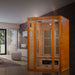 Golden Designs Maxxus Aspen Dual Tech 2 Person Low EMF Far Infrared Sauna stands in a modern living room with tall windows and a white ottoman