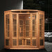 Golden Designs Maxxus Avignon 3 Person Corner Near Zero EMF Far Infrared Sauna in Red Cedar glows with accent lights in a dark modern room beside a gray sofa