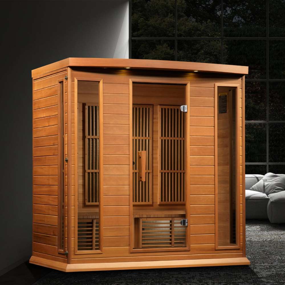 Golden Designs Maxxus Chaumont 4 Person Near Zero EMF Far Infrared Sauna in Red Cedar glows with accent lights in a dark modern room beside a gray sofa