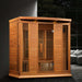 Golden Designs Maxxus Chaumont 4 Person Near Zero EMF Far Infrared Sauna in Red Cedar glows with accent lights in a dark modern room beside a gray sofa