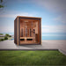 Golden Designs Visby 3 Person Outdoor-Indoor PureTech Hybrid Full Spectrum Sauna sits on a gray patio beside green grass with the sea and a blue sky behind it