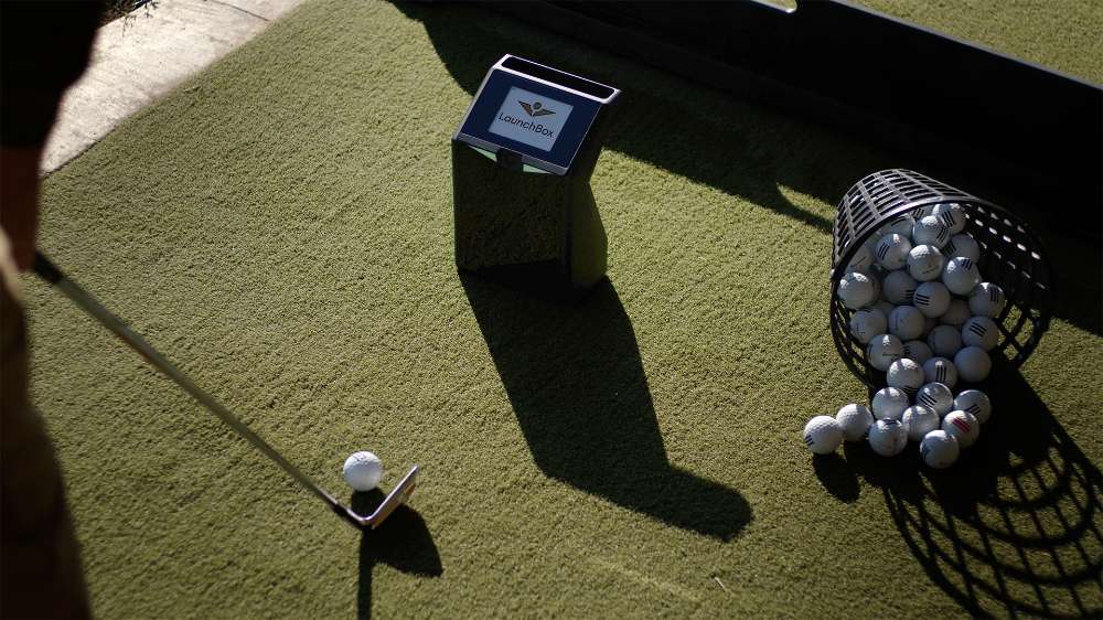 Golfer hits a ball indoors while the launch monitor tracks the shot using TruGolf LaunchBox Golf Launch Monitor w/ Starter 10 (2025) Enclosure + Gimme Package