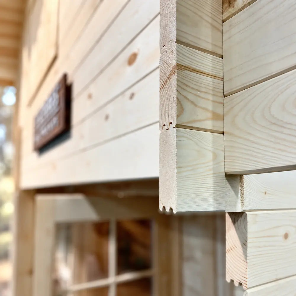 Close-up of the Grand Loft 107 Deluxe DD interlocking timber corner joint, showing precisely cut unfinished wood profiles and grain.