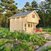 Angled forest view of the Grand Loft 107 Deluxe DD cabin with a steep metal roof, upper loft window, glazed doors and red porch chairs.