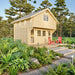 Front view of the Grand Loft 107 Deluxe DD wooden cabin with a steep metal roof, loft window, glazed doors and two red Adirondack chairs.