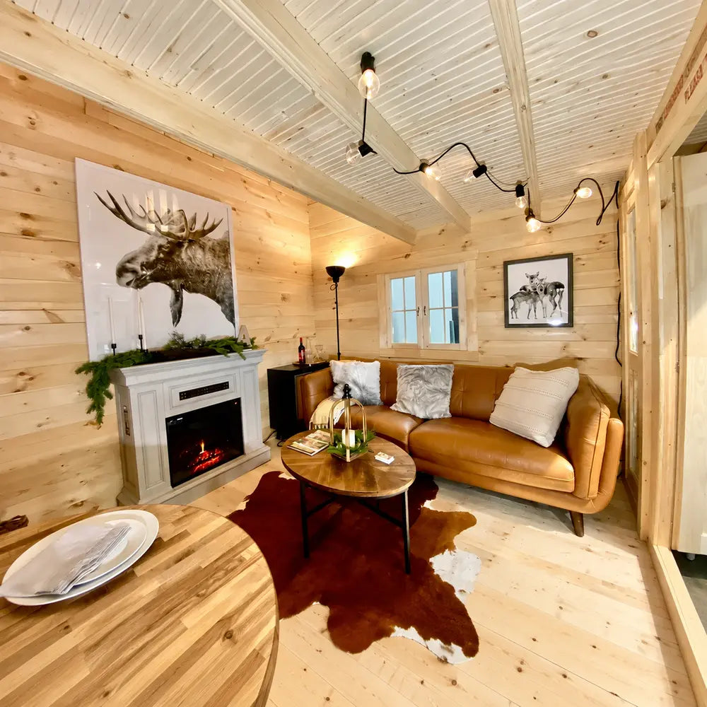 Grand Loft 107 Deluxe DD living room with warm wood walls, a brown leather sofa, cowhide rug, fireplace and large moose artwork.