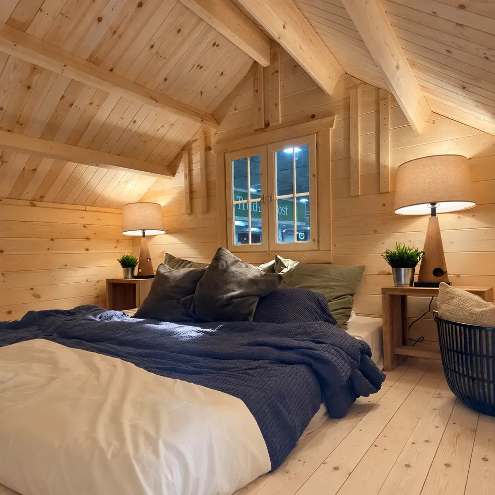 Grand Loft 107 Deluxe DD loft bedroom with a double bed, dark blue bedding, matching bedside lamps and a sloped wood-paneled ceiling.