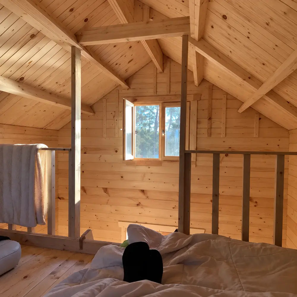 Sunlit upstairs loft in the Grand Loft 107 Deluxe DD, with an open window, wood-paneled walls, exposed beams and bedding in the foreground.
