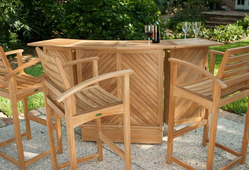 Group of Westminster Teak Somerset Teak Bar Stools surrounds a wooden outdoor bar table holding wine glasses and a bottle
