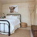 Cozy Harvest Grand Bungalow bedroom with a black metal bed, white bedding, woven poufs and a wall-mounted Highland cow portrait.