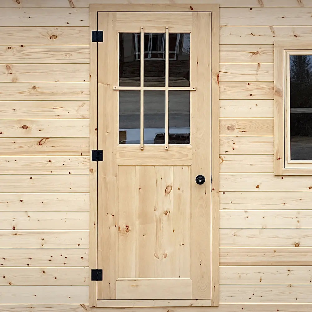 Solid pale-wood exterior door with a six-pane window grid, black hinges and a round black handle on the Harvest Grand Bungalow.