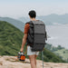 Hiker wears Jackery SolarSaga 40 Air Solar Panel attached to a backpack while carrying a portable power station through the mountains
