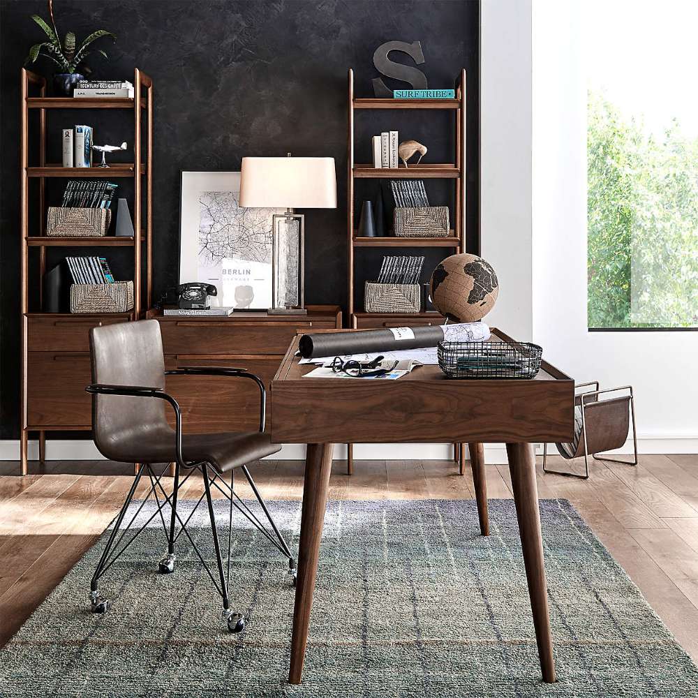 Home office with a wooden desk and shelving units, featuring Crate & Barrel Tate Walnut Lateral File Cabinet beneath a lamp and framed artwork against a dark accent wall