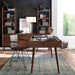 Home office with a wooden desk and shelving units, featuring Crate & Barrel Tate Walnut Lateral File Cabinet beneath a lamp and framed artwork against a dark accent wall
