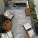 In a cozy patio setup, Couristan Dolce Indoor/Outdoor Rug - Flora/Argento anchors wooden furniture and surrounds a small pond