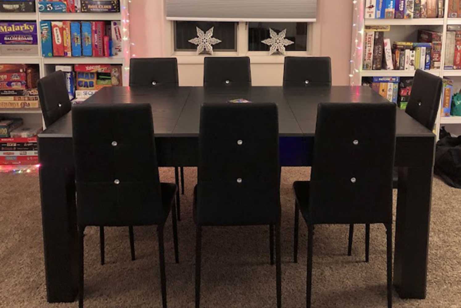 In a festive game room setup, the Game Theory Tables Origins Modular Large Game Table is surrounded by eight black chairs