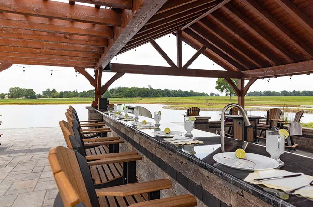 Inside the Brookside Timber Frame Combolan Estate Pavilion, a well-designed outdoor bar and dining area create a luxurious space