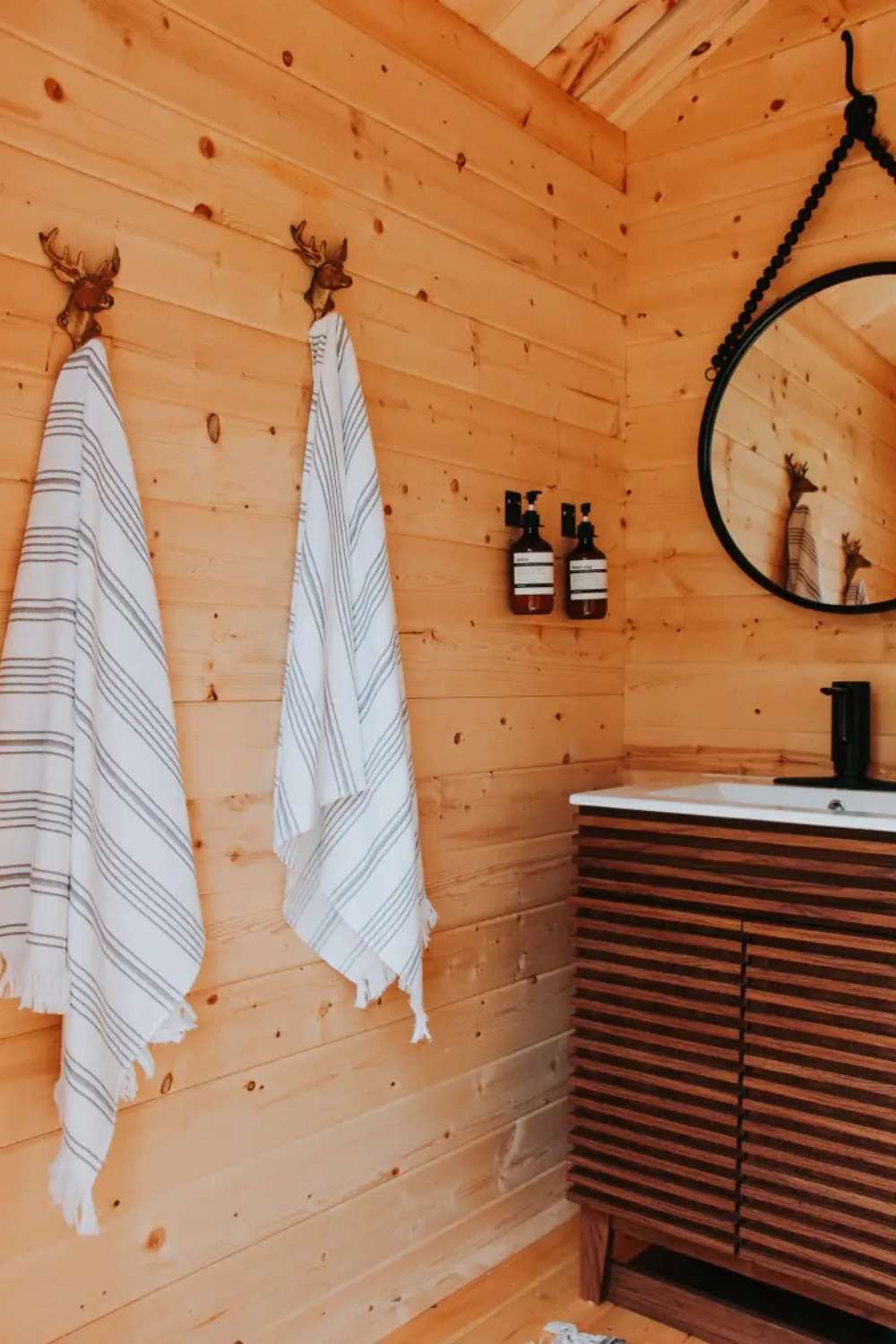 Inside Sawmill Structures Loo Loo House Garden Room striped towels hang neatly on antler hooks next to a modern wooden vanity with soap dispensers