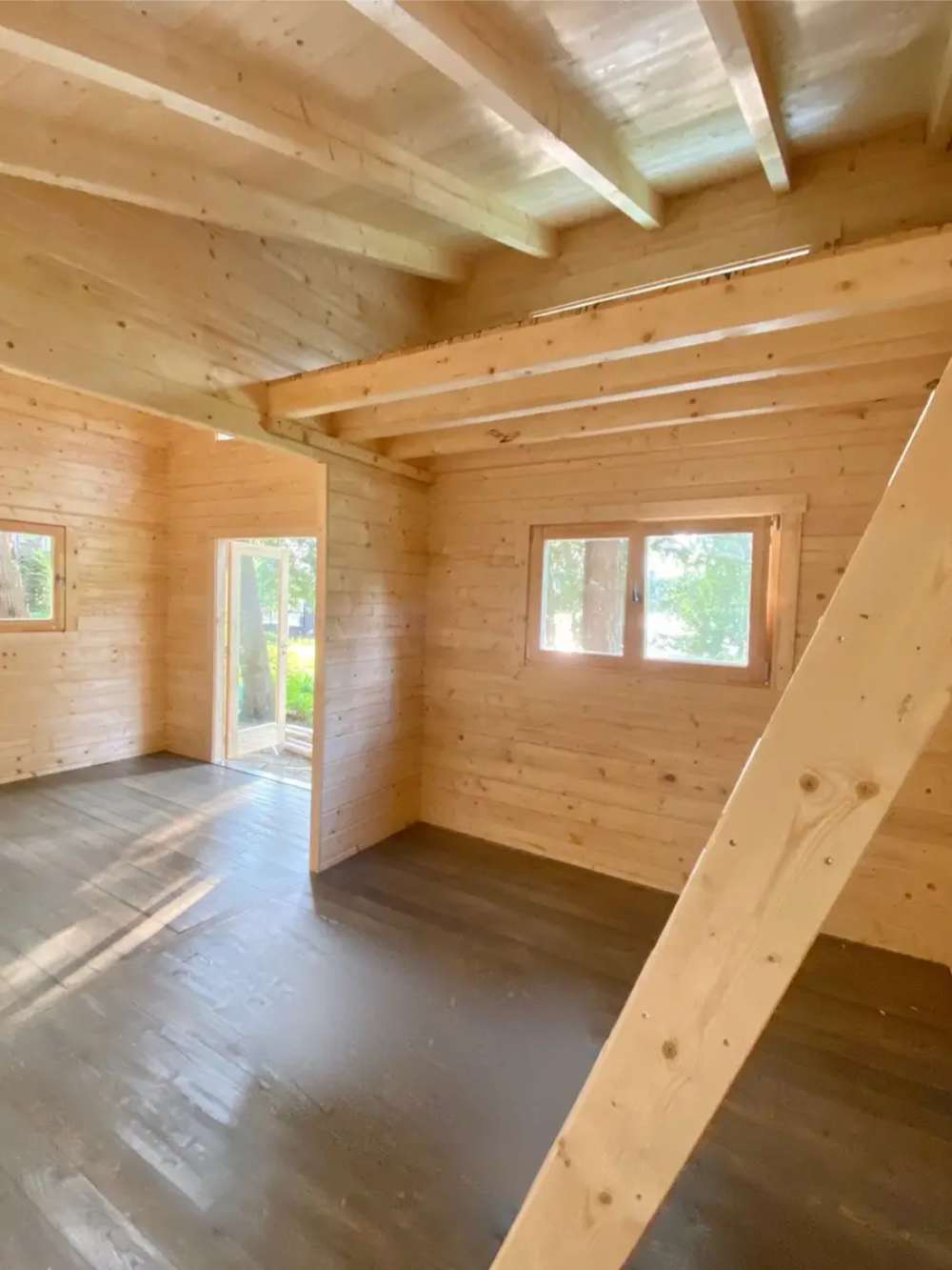 Inside Sawmill Structures The Versa 240 70MM Garden Room, wooden beams stretch overhead above a bright open area with multiple windows