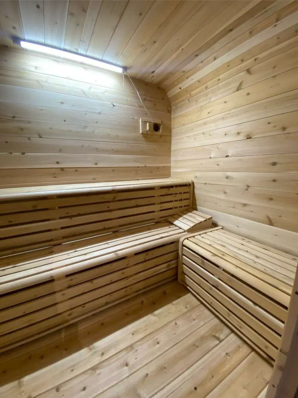 Inside of Sawmill Structures Box Sauna with light wood paneling and two-tier bench seating that wraps around the walls
