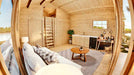 Inside the Sawmill Structures Edwin Lake House 70MM Garden Room, a cozy living space features a couch, rug, small round table, and a compact kitchen along one wall
