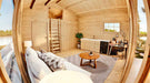 Inside the Sawmill Structures Edwin Lake House 70MM Garden Room, a cozy living space features a couch, rug, small round table, and a compact kitchen along one wall