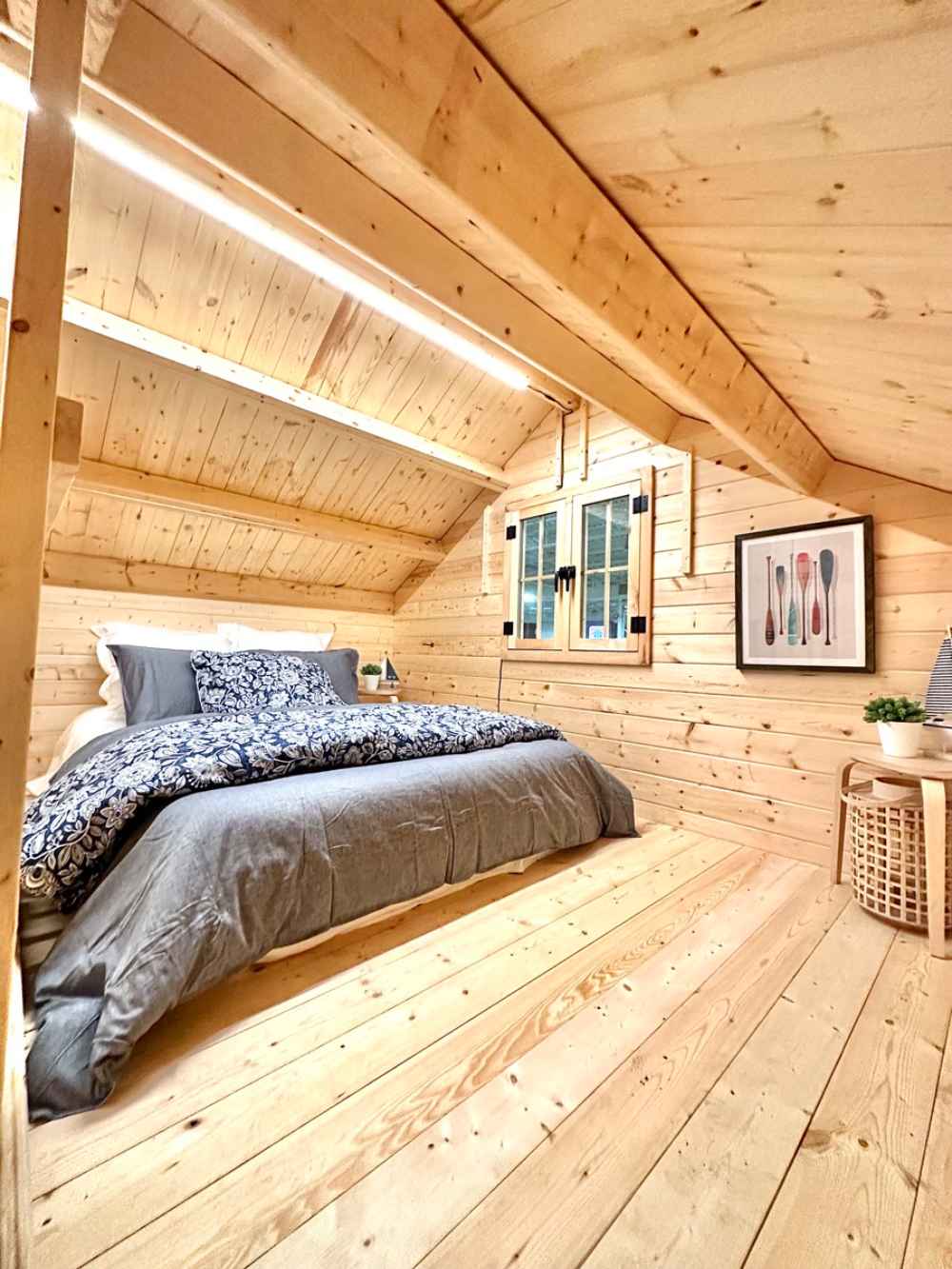 Inside the Sawmill Structures Ontario Grand Loft 107 SD Garden Room, a cozy loft bedroom features natural wood walls, slanted ceiling, and a double bed