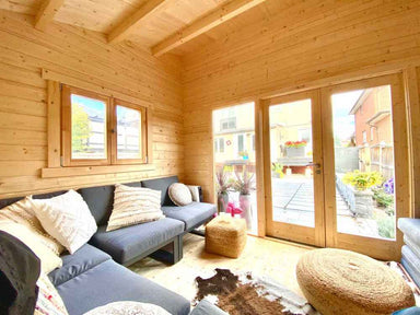 Inside the Sawmill Structures The Versa 107 70MM Garden Room, cozy seating with plush pillows and poufs faces the bright glass doors and garden view