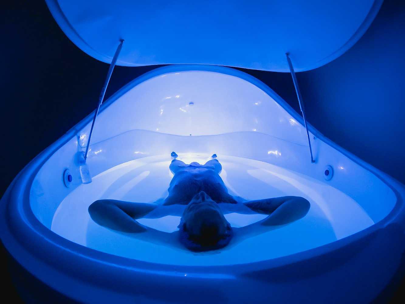 Inside view of the Dreampod Vmax Float Pod with a person floating in glowing blue water