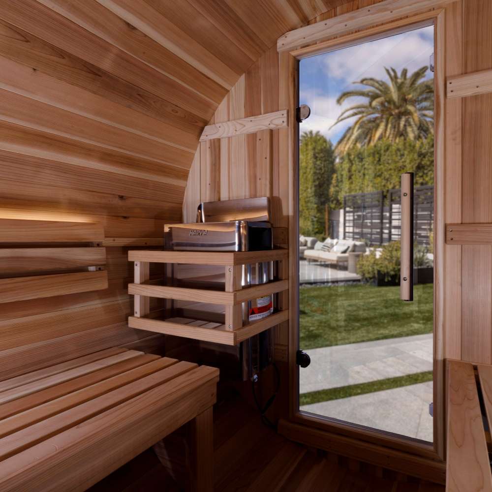 Interior of Golden Designs Zurich 4 Person Barrel with Bronze Privacy View Traditional Sauna showing curved cedar walls, a lit backrest and the stove with stones in a wood guard