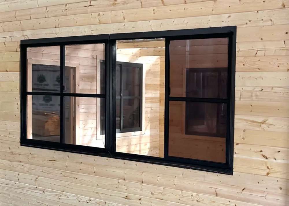 Interior of Sawmill Structures Eze Breeze Sunroom Cabin shows a black-framed sliding window on a smooth pine wall