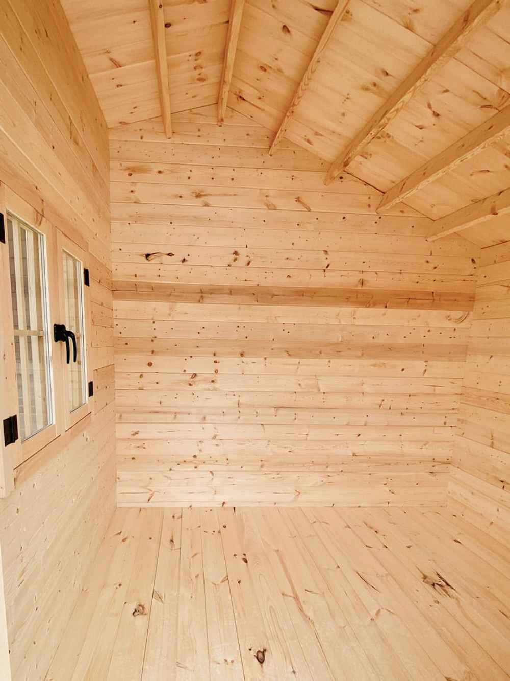 Interior of the Sawmill Structures Bluewater Den 67 Garden Room, with natural pine wood walls, a pitched roof, and visible rafters